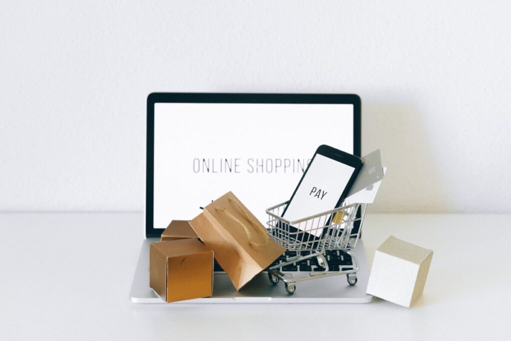 écran ordinateur avec écrit online shopping et téléphone portable dans un caddy