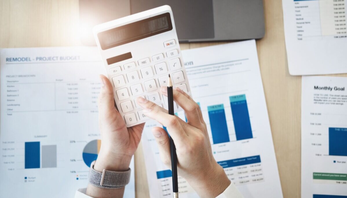 budget-communication-marketing Mains qui tiennent une calculette avec des feuilles à l'arrière