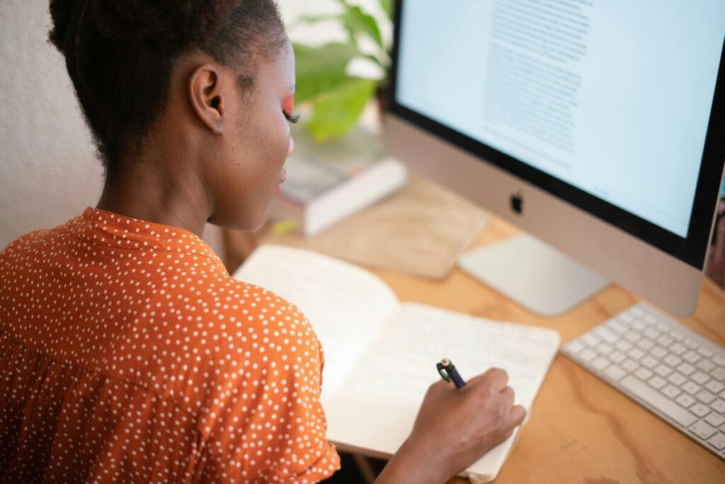 Femme copywriter devant un écran d'ordinateur qui écrit sur un carnet de notes