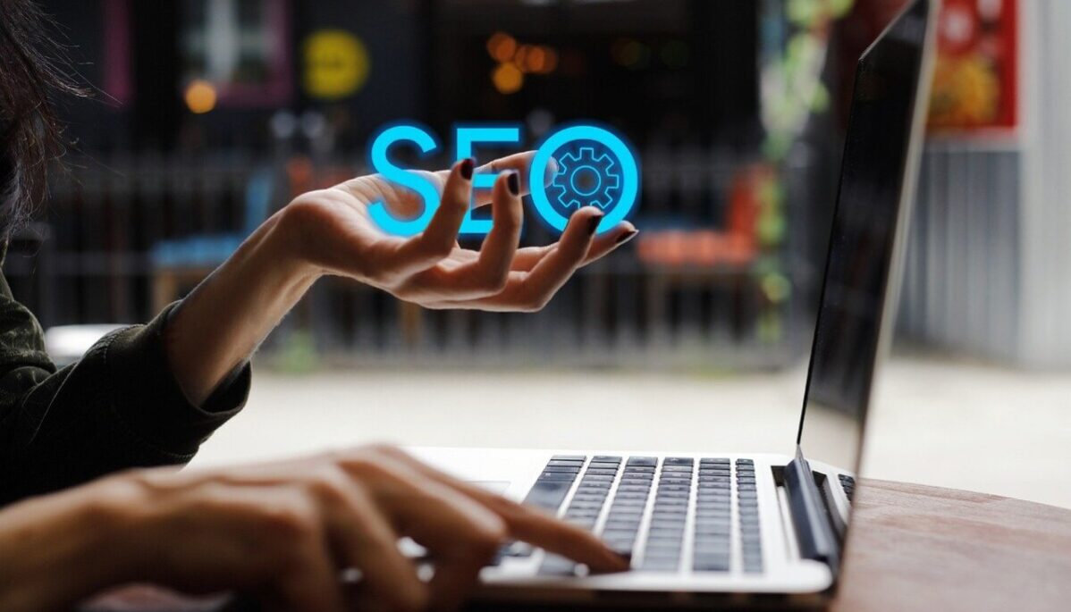 Femme devant un ordinateur portable qui tient dans sa main gauche les lettres SEO en bleu