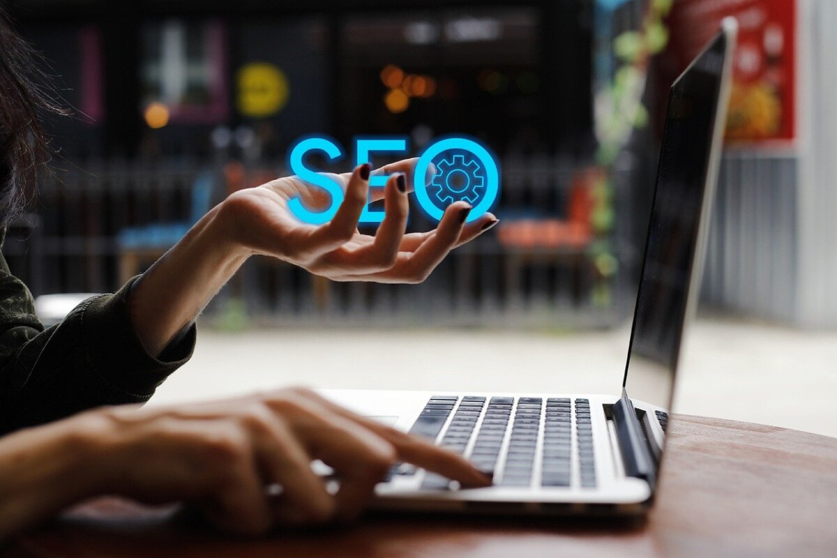 Femme devant un ordinateur portable qui tient dans sa main gauche les lettres SEO en bleu