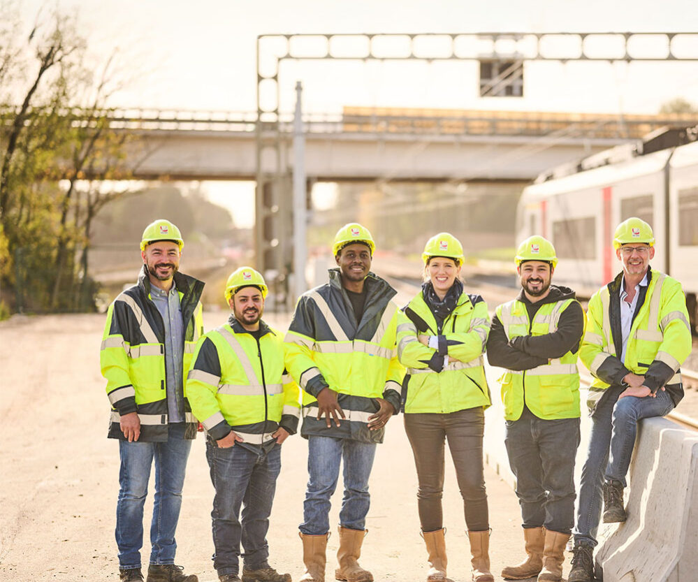tuc-rail-equipe Des ingénieurs en tenue de travail sur un chantier. Ils portent tous des gilets de sécurité haut visibilité de couleur jaune fluo.