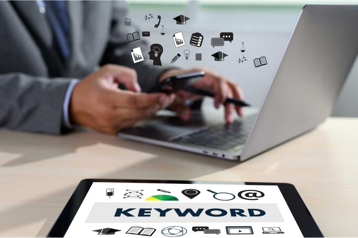 Un homme utilise son smartphone et son ordinateur portable, entouré d'icônes de communication et d'éducation. À côté, une tablette affiche 'KEYWORD' avec des icônes de recherche et gestion.