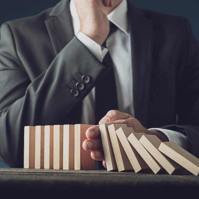 Homme en costume arrête la chute de dominos en bois pour symboliser la gestion de crise pour protéger l'image de marque